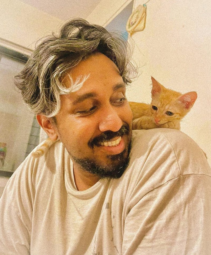 Nilesh laughing while Mineu, an orange kitten, perches on his shoulder