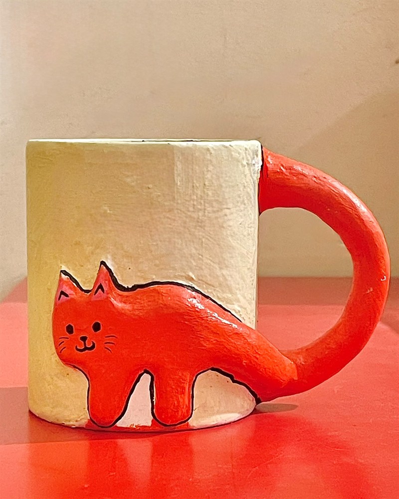 Handmade white mug with an orange cat wrapped around it, its tail forming the handle